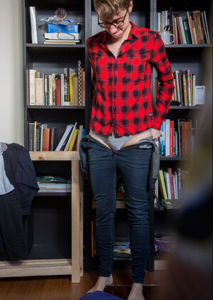 Undressed short-haired girl with glasses puts clothes on right in the library